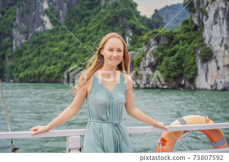 Attractive woman in a dress is traveling by boat in Halong Bay. Vietnam. Travel to Asia, happiness emotion, summer holiday concept. Picturesque sea landscape. Ha Long Bay, Vietnam 73807592