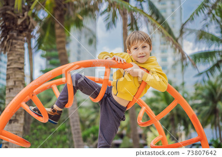 The boy climbs on the playground against the background of palm trees The boy climbs on the playground against the background of palm trees 73807642