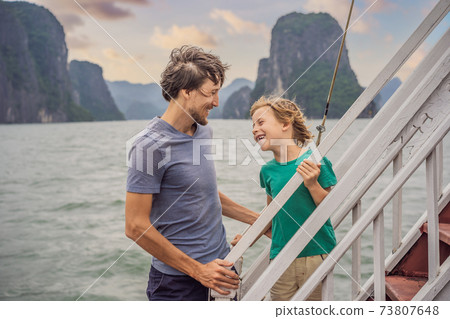 Father and son travelers is traveling by boat in Halong Bay. Vietnam. Travel to Asia, happiness emotion, summer holiday concept. Traveling with children concept. After COVID 19. Picturesque sea Father and son travelers is traveling by boat in Halong Bay. Vietnam. Travel to Asia, happiness emotion, summer holiday concept. Traveling with children concept. After COVID 19. Picturesque sea 73807648