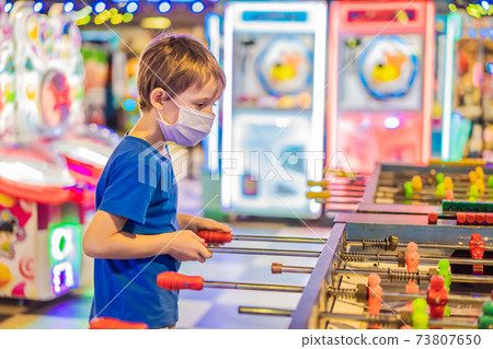 Little blond boy wearing a medical mask during COVID-19 coronavirus playing board table soccer Little blond boy wearing a medical mask during COVID-19 coronavirus playing board table soccer 73807650