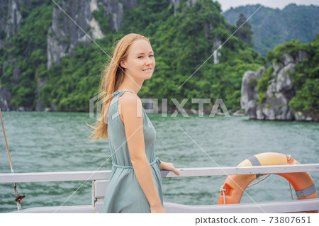Attractive woman in a dress is traveling by boat in Halong Bay. Vietnam. Travel to Asia, happiness emotion, summer holiday concept. Picturesque sea landscape. Ha Long Bay, Vietnam Attractive woman in a dress is traveling by boat in Halong Bay. Vietnam. Travel to Asia, happiness emotion, summer holiday concept. Picturesque sea landscape. Ha Long Bay, Vietnam 73807651