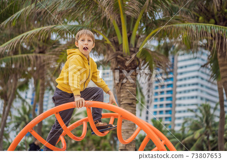 The boy climbs on the playground against the background of palm trees The boy climbs on the playground against the background of palm trees 73807653