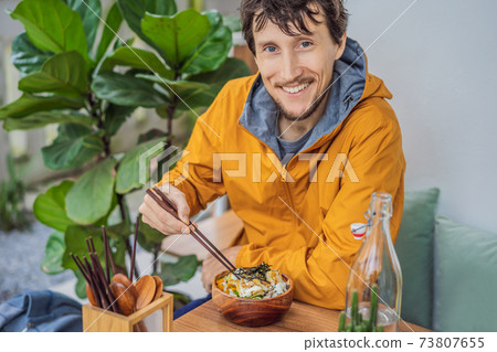 Man eating Raw Organic Poke Bowl with Rice and Veggies close-up on the table. Top view from above horizontal Man eating Raw Organic Poke Bowl with Rice and Veggies close-up on the table. Top view from above horizontal 73807655