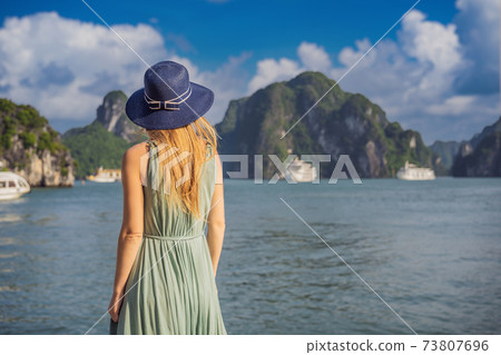 Attractive woman in a dress is traveling in Halong Bay. Vietnam. Travel to Asia, happiness emotion, summer holiday concept. Picturesque sea landscape. Ha Long Bay, Vietnam 73807696