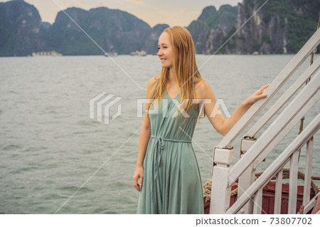 Attractive woman in a dress is traveling by boat in Halong Bay. Vietnam. Travel to Asia, happiness emotion, summer holiday concept. Picturesque sea landscape. Ha Long Bay, Vietnam Attractive woman in a dress is traveling by boat in Halong Bay. Vietnam. Travel to Asia, happiness emotion, summer holiday concept. Picturesque sea landscape. Ha Long Bay, Vietnam 73807702
