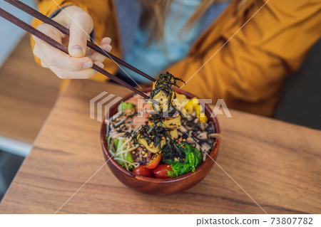 Woman eating Raw Organic Poke Bowl with Rice and Veggies close-up on the table. Top view from above horizontal 73807782