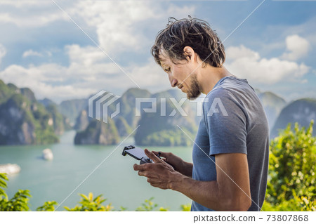 Man controls a drone in Halong Bay. Vietnam. Travel to Asia, happiness emotion, summer holiday concept. Picturesque sea landscape. Ha Long Bay, Vietnam Man controls a drone in Halong Bay. Vietnam. Travel to Asia, happiness emotion, summer holiday concept. Picturesque sea landscape. Ha Long Bay, Vietnam 73807868