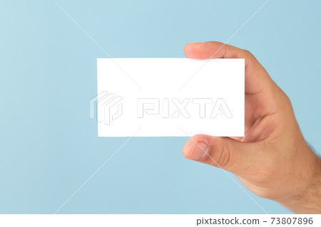 Male hand holding blank business card on light blue background Male hand holding blank business card on light blue background 73807896