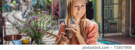 BANNER, LONG FORMAT Young woman traveler drinks coffee sitting by the railway paths which go through residential area in Hanoi city. Hanoi Train Street is a famous tourist destination. Vietnam reopens 73807906