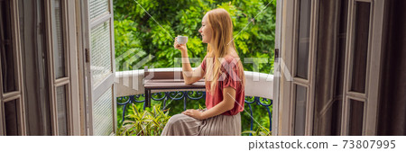 BANNER, LONG FORMAT A ginger-haired woman stands on a heritage-style balcony enjoying her morning coffee. A woman in a hotel in Europe or Asia as tourism recovers from a pandemic. Tourism has BANNER, LONG FORMAT A ginger-haired woman stands on a heritage-style balcony enjoying her morning coffee. A woman in a hotel in Europe or Asia as tourism recovers from a pandemic. Tourism has 73807995