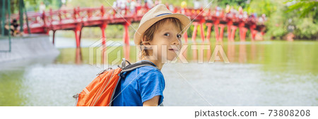 BANNER, LONG FORMAT Caucasian boy tourist on background of Red Bridge in public park garden with trees and reflection in the middle of Hoan Kiem Lake in Downtown Hanoi. Traveling with children concept 73808208