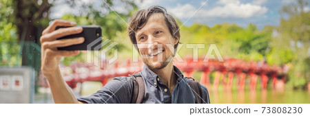 BANNER, LONG FORMAT Caucasian man traveler on background of Red Bridge in public park garden with trees and reflection in the middle of Hoan Kiem Lake in Downtown Hanoi. Vietnam reopens after BANNER, LONG FORMAT Caucasian man traveler on background of Red Bridge in public park garden with trees and reflection in the middle of Hoan Kiem Lake in Downtown Hanoi. Vietnam reopens after 73808230