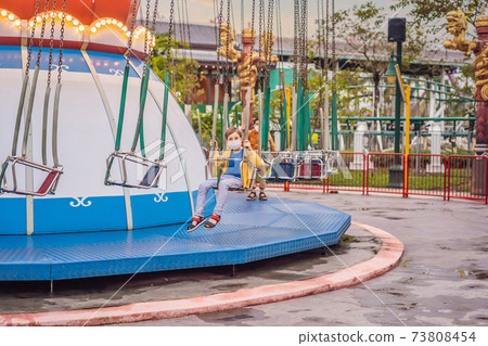 Father and son riding a carousel wearing a medical mask during COVID-19 coronavirus 73808454