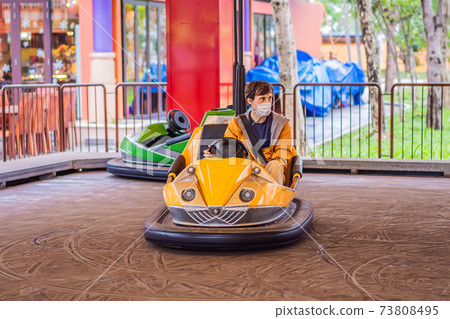 Man wearing a medical mask during COVID-19 coronavirus having a ride in the bumper car at the amusement park 73808495