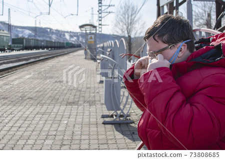 the man adjusts the mask on his face and waits for the train 73808685
