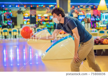 Man playing bowling with medical masks during COVID-19 coronavirus in bowling club 73808836