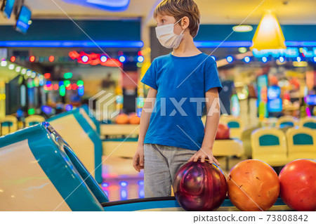 Boy playing bowling with medical masks during COVID-19 coronavirus in bowling club Boy playing bowling with medical masks during COVID-19 coronavirus in bowling club 73808842
