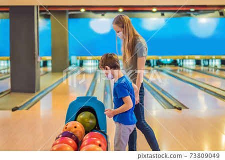 beautiful young mother and son playing bowling with medical masks during COVID-19 coronavirus in bowling club 73809049
