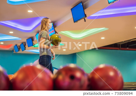 Woman playing bowling with medical masks during COVID-19 coronavirus in bowling club 73809094