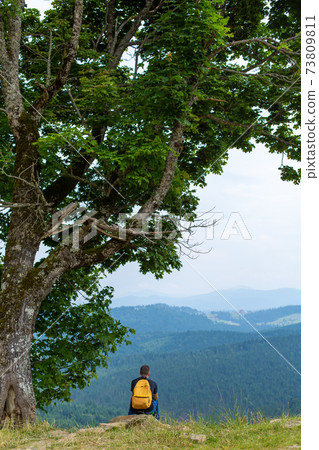 Alone guy sitting on cliff and enjoy peaceful green mountains landscape. Peace of mind and relax 73809811