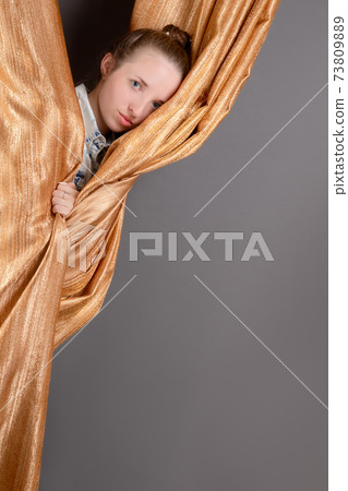 The girl makes plans for the arrangement of her new apartment. Photo of a girl in gold curtains with blank copy space 73809889