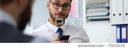 Smiling young businessman holding mobile phone in arm Smiling young businessman holding mobile phone in arm 73810250