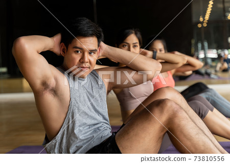 Group of Asian women and man doing abdominal exercises on yoga mats in aerobics class. Young sporty people twisting body on the floor in gym studio. 73810556