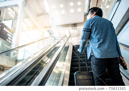 Male tourist carrying suitcase luggage on escalator 73811501