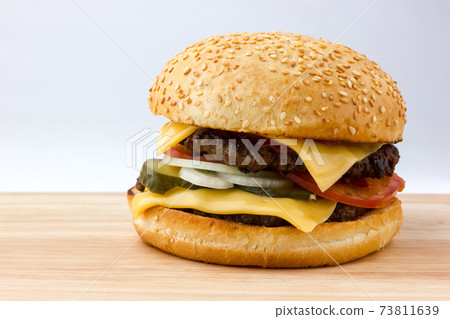 Burger close-up on a wooden table. A large burger with a beef cutlet, tomatoes, cheese, pickled cucumbers and onions on a wooden table. Burger close-up on a wooden table. A large burger with a beef cutlet, tomatoes, cheese, pickled cucumbers and onions on a wooden table. 73811639