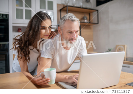 Woman hugging her husband while he is checking mails Woman hugging her husband while he is checking mails 73811837