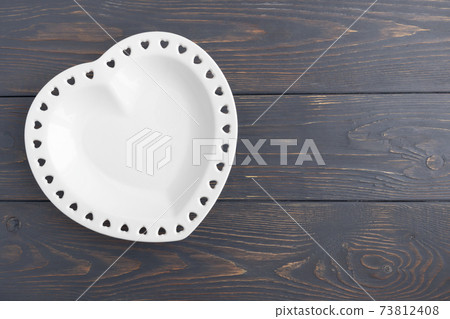 White plate in the shape of a heart on a gray wooden background with space for text. Layout for your postcard or advertisement. 73812408