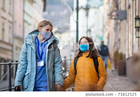 Woman healthcare worker outdoors on the way to work with schoolgirl daughter, coronavirus concept. Woman healthcare worker outdoors on the way to work with schoolgirl daughter, coronavirus concept. 73812525