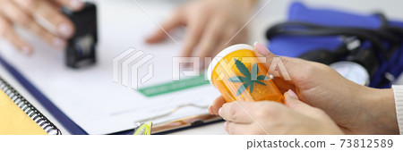 Patient holding jar of marijuana in hands. Doctor putting stamp on document Patient holding jar of marijuana in hands. Doctor putting stamp on document 73812589