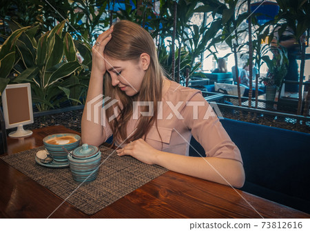 Heartbroken young lady is sitting in cafe and thinking regretfully 73812616