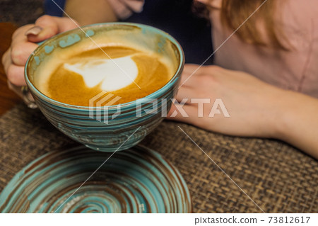 Mug of coffee over the sourcer, the girl holds in her hand one cup of milk coffee in an air. A photo depicting a cosy relaxing coffeebreak Mug of coffee over the sourcer, the girl holds in her hand one cup of milk coffee in an air. A photo depicting a cosy relaxing coffeebreak 73812617