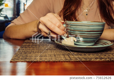 Cup of coffee on a wooden table, the girl holds her hand one cup of coffee . A photo depicting a melancholic mood 73812626