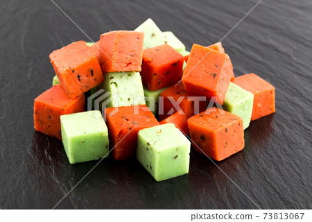 Cheese cubes of red and green color on a slate board. Cheese pesto closeup on the surface of the stone. 73813067