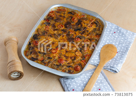 Casserole in a baking tray on a wooden table. The finished dish is baked in the oven. 73813075