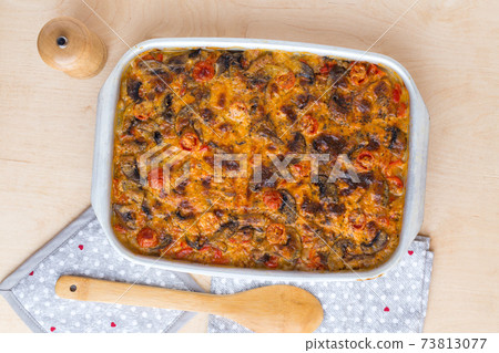 Casserole in a baking tray on a wooden table. The finished dish is baked in the oven. 73813077