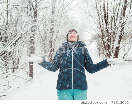 Smiling woman is playing with snow. Fun in snowy winter forest. Woman laughs as she walks through wood. Sincere emotions. 73813605
