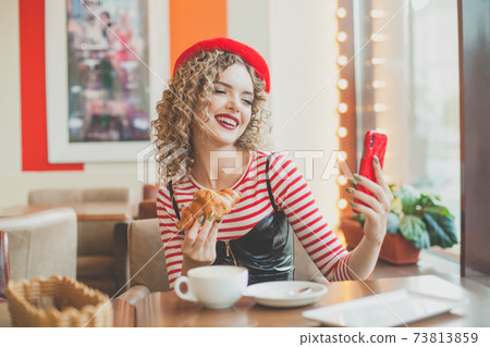 Happy pretty woman using smartphone and taking selfie in european city street cafe 73813859
