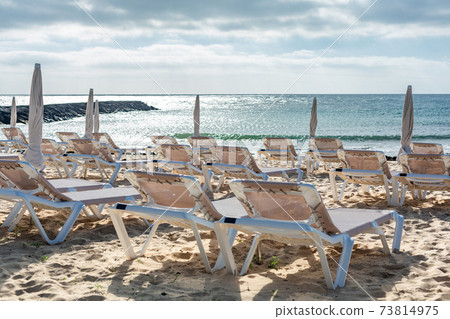 Empty chaise-lounges on the beach in the city of Costa Teguise. Empty chaise-lounges on the beach in the city of Costa Teguise. 73814975