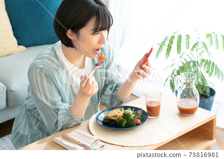 A woman eating while watching a smartphone 73816981