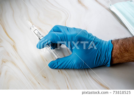 Doctors hands hold syringe with liquid medicine in it, preparing for vaccination. Healthcare concept. Protection from viruses, medical mask, coronavirus. Blurred background.  73818525