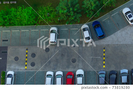 Above view of cars parked at car parking area of the apartment. Aerial view concrete car parking lot with speed bump near green trees in the park. Outdoor car parking space with empty slots. Above view of cars parked at car parking area of the apartment. Aerial view concrete car parking lot with speed bump near green trees in the park. Outdoor car parking space with empty slots. 73819280