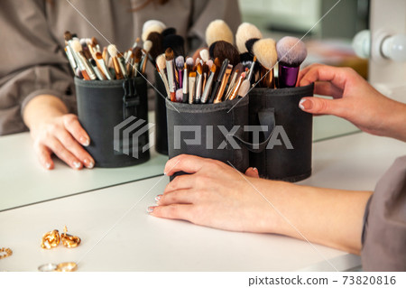 Woman hands is taking out makeup brush set from the drawer of vanity table. 73820816