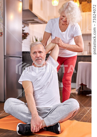 senior couple exercising at home, woman help husband to stretch senior couple exercising at home, woman help husband to stretch 73824072