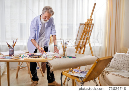 senior artist draws a sketch on paper, and then on canvas senior artist draws a sketch on paper, and then on canvas 73824748
