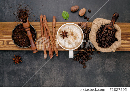 Roasted coffee beans with coffee powder and flavourful ingredients for make tasty coffee setup on dark stone background. 73827295