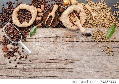 Background of various coffee , dark roasted coffee beans , ground and capsules with scoops setup on wooden background with copy space. Background of various coffee , dark roasted coffee beans , ground and capsules with scoops setup on wooden background with copy space. 73827333